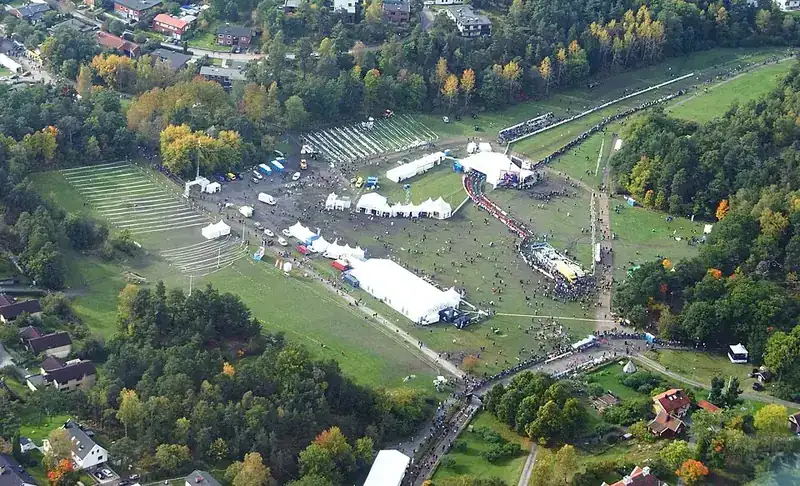 Terränglopp sett uppifrån med tältby, publik och löpare på en slinga genom kuperad mark